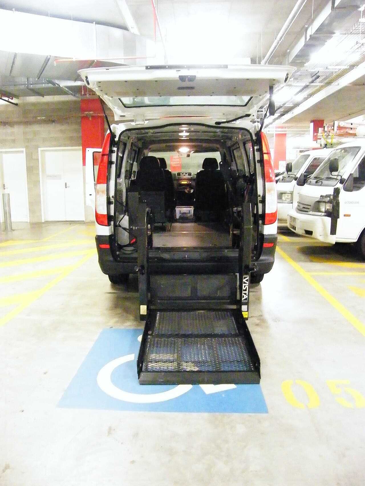 A heavy powered wheelchair being raised with a platform lift at the side door of an accessible van