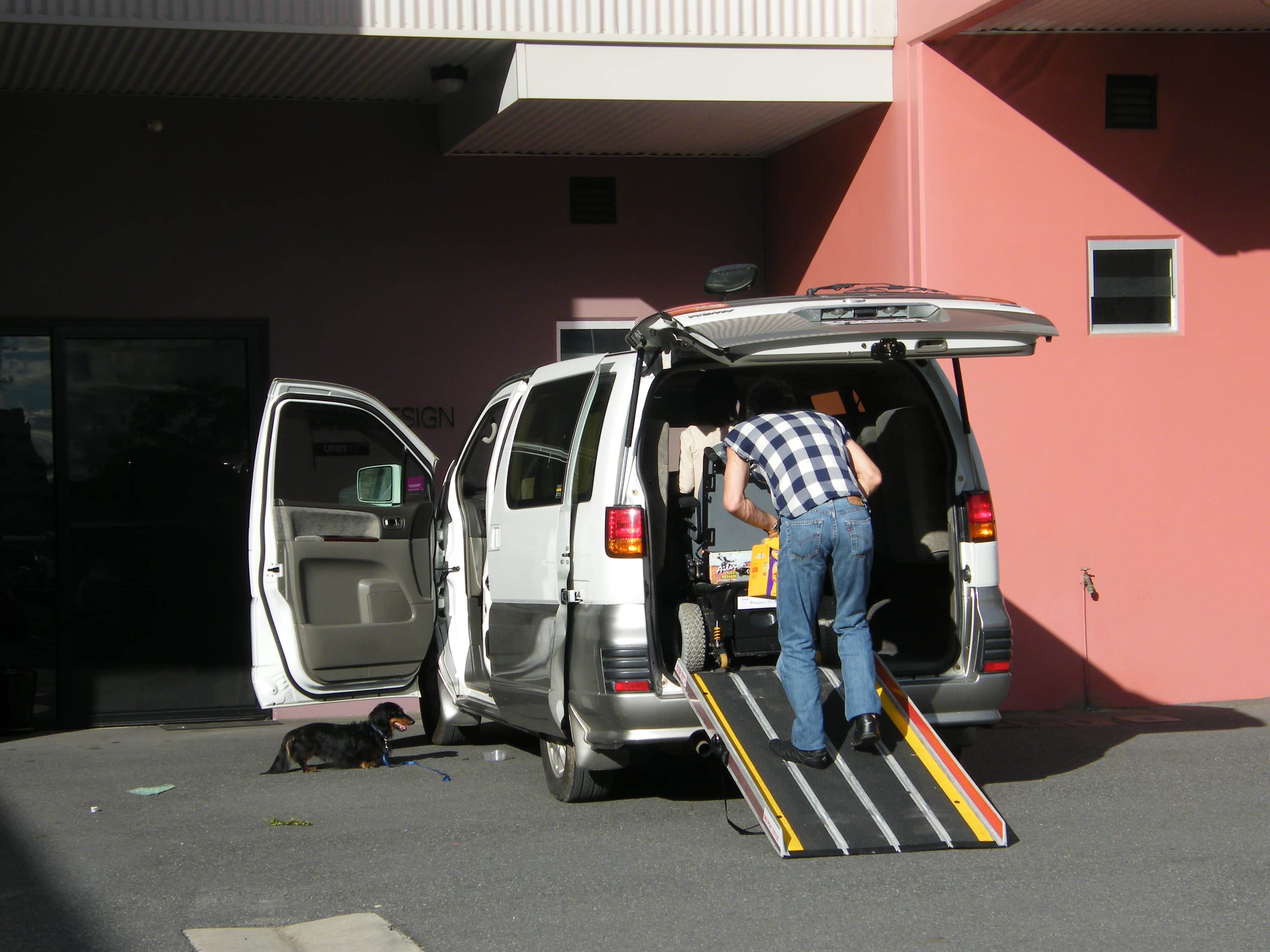 A folded wheelchair being guided up a portable ramp into an SUV cargo area