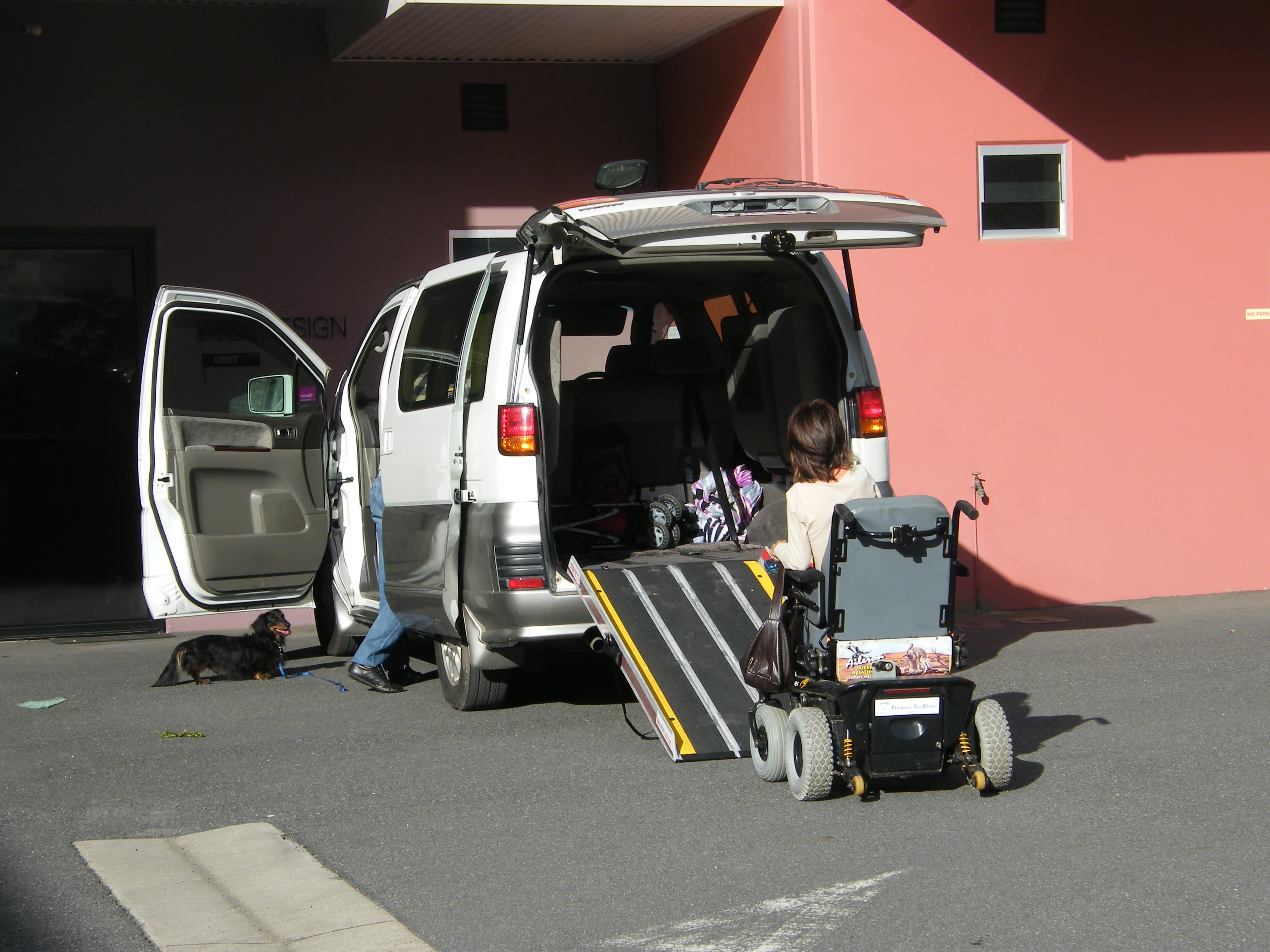 A powered wheelchair and portable ramp positioned at the rear cargo opening of a vehicle